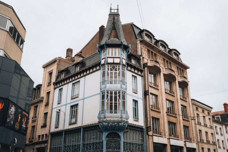 This is the top half of the Ancienne Graineterie Génin in Nancy. The ironwork has a flowery design and there are a few stained glass windows in the middle that have an art nouveau style.