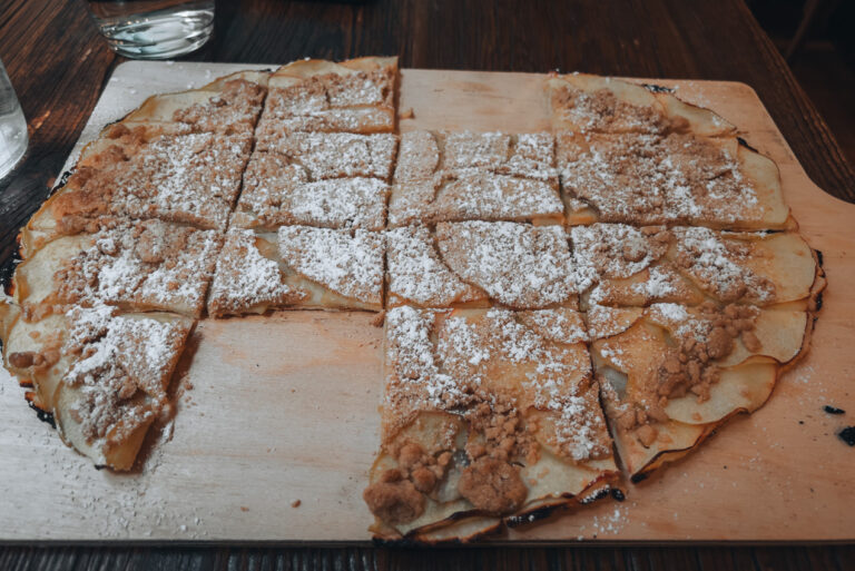 Appel Strudel Tarte Flambée from La Soi in Colmar. It's topped with thin apple slices, strudel, and powdered sugar. Two slices have already been eaten.