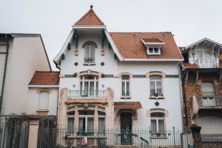 This is an Art Nouveau Building on Rue Felix Faure in Nancy. It's a while building with seven windows and one door. There are decorations around the windows with different color bricks.