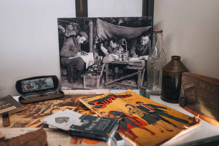 Artifacts, including a photo, a superman comic book, glasses, playing cards, and a coca cola bottle, from American Soldiers at the Musée Mémorial des Combats de la Poche de Colmar.