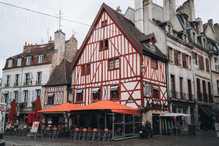This is Au Moulin à Vent in Place François Rude. It's a red timber framed building with a awning. Under the awning there are tables and chairs. 