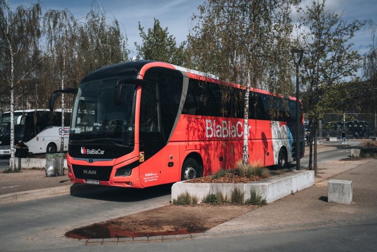 This is a BlaBlaCar Bus parked at the bus station in Strasbourg. It's a large pink bus with the word BlaBla Car written on the front. 