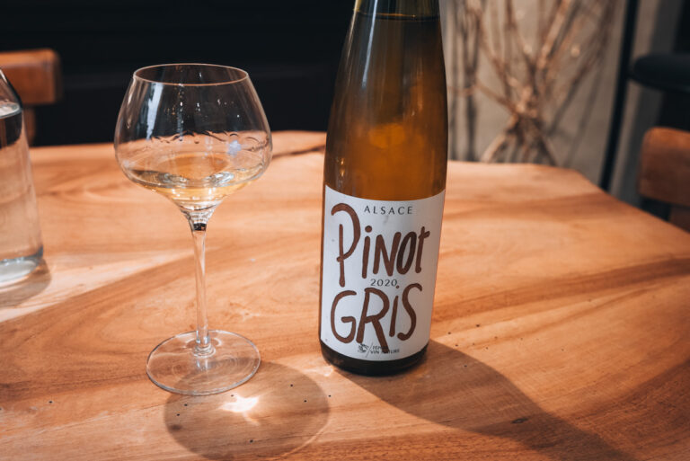 Bottle of Pinot Gris from Domaine Martin Jund next to a half filled wine glass on a wooden table. Wine tasting is one of the top things to do during the winter season in Alsace.