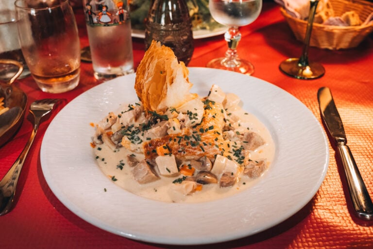 Traditional Bouchée à la Reine served in a ceramic dish filled with creamy sauce, chicken, and mushrooms on a dining table in Alsace. This classic regional dish is part of the culinary experience along an Alsace wine route.