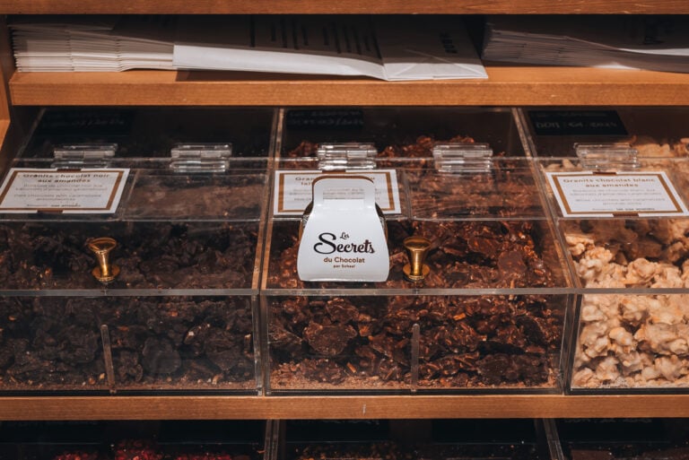 This is a photo of my box of chocolate that I got from Musée du Chocolat par Schaal. It's a small white box with the name of the museum written on the front. It's sitting on a clear box of chocolate candy from the museum.