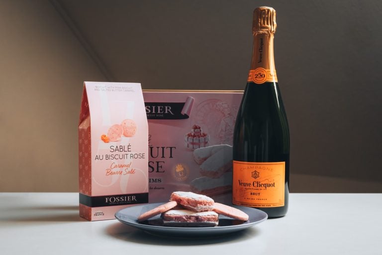 This is a bottle of Veuve Clicquot Champagne and Fossier Biscuits from Reims. There are two boxes of biscuits and one bottle of champagne. In front there are four biscuits on a dish.