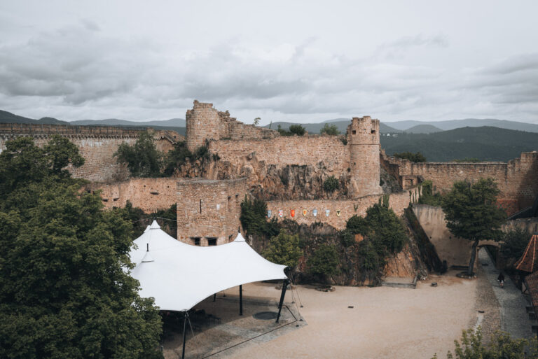 Outer walls and towers of the Château du Hohlandsbourg in Alsace. It's surrounded by trees and in the distance the Vosges mountains.