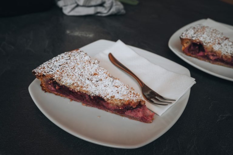 This is a cherry tart from the Patisserie au Petit Kougelhopf in Wissembourg. It's on white square plate and topped with powered sugar. Then on the right there is a fork on a napkin.