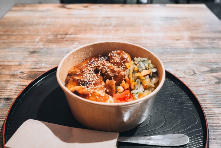 This is my chicken teriyaki bowl from Au Petit Japon at the Marché Central de Nancy in Nancy. It's a bowl with chicken, vegetables, and rise. It's on a small round tray with a fork and napkin.