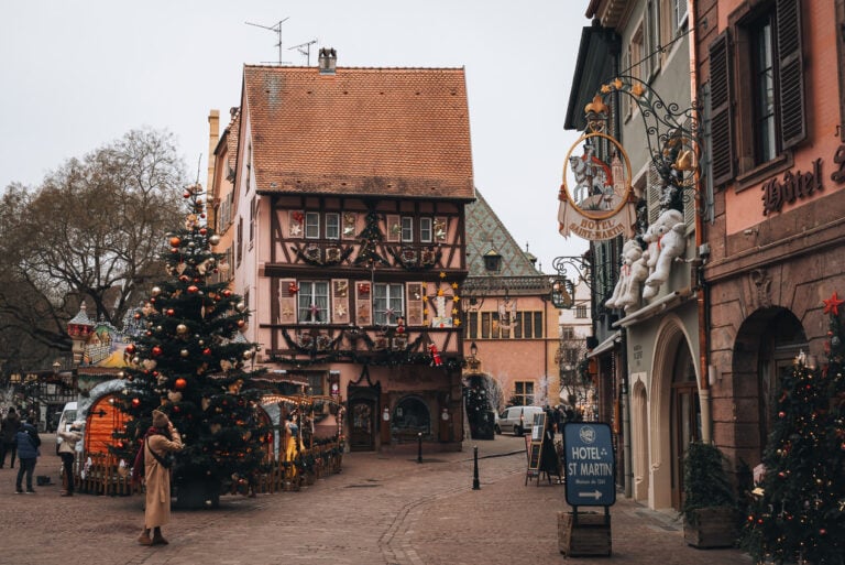 This is Grand Rue in Colmar at Christmas. There is a half-timbered house and a tree decorated with ornaments and lights. It's one of the best Christmas markets in Alsace.