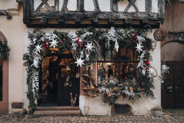 The entrance of a shop in Riquewihr that is decorated in wreaths, ornaments, and lights for the Christmas market.