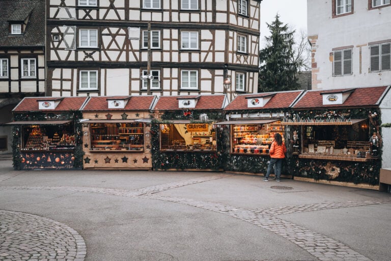 This is a series of five Christmas market stalls at Place de l'Ancienne Douane in Colmar. Each one is selling different Christmas related items and there is one person shopping.