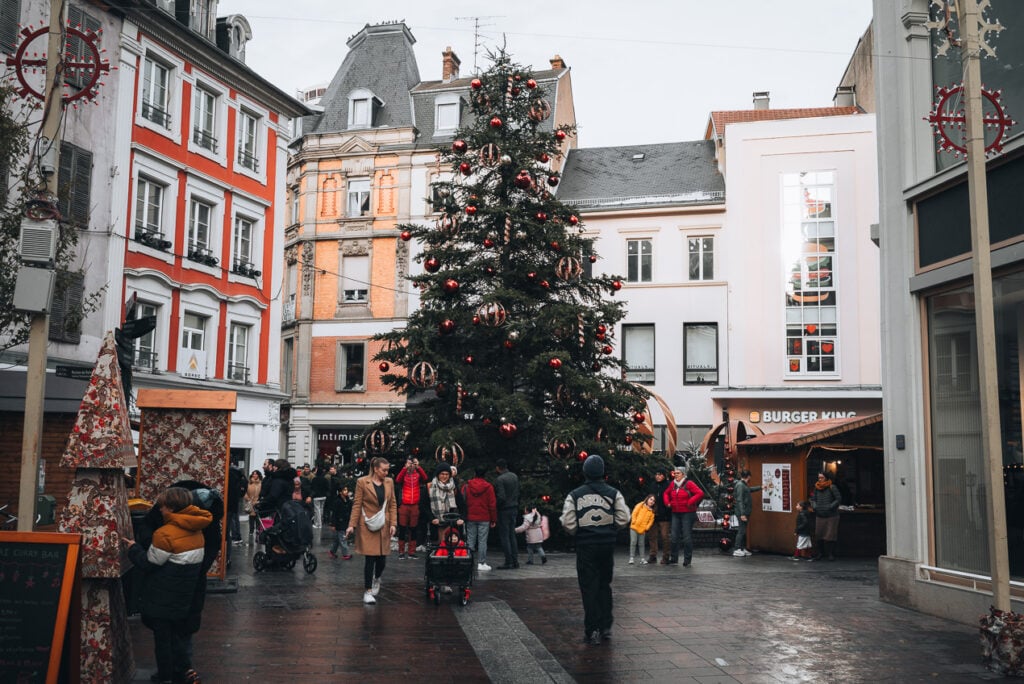 This is the Christmas tree in Place des Victoires in Mulhouse. It's a giant tree decorated with ornaments and people are walking around it.