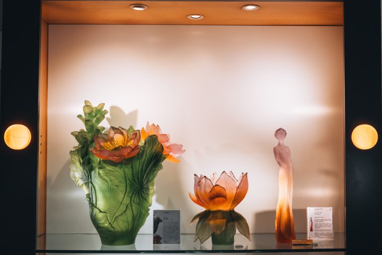 This is a collection of three pieces of Daum glassware at the Daum store in Nancy. On the far left, there is a large pot with flowers. In the middle there is a small flower, and on the far right, it's a silhouette of a young woman.