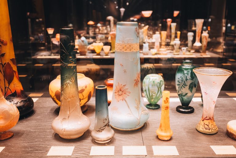 Daum glassware exhibit at the Musée des Beaux Arts in Nancy. There are four vases in view, each decorated with floral designs. Then, behind those, you can see a large collection of vases.