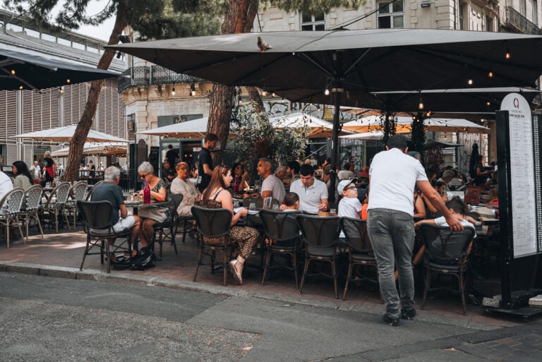 This is an outdoor terrace in Montpellier. People are sitting at tables talking quietly to each other.