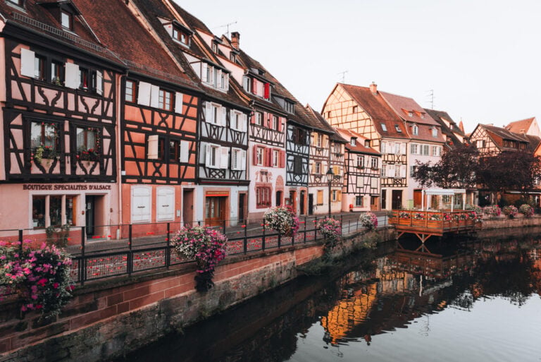 Quiet early morning street scene on Rue des Écoles in Colmar with soft light reflecting on half timbered buildings and empty cobblestone streets. The peaceful atmosphere captures a calm moment in Alsace.