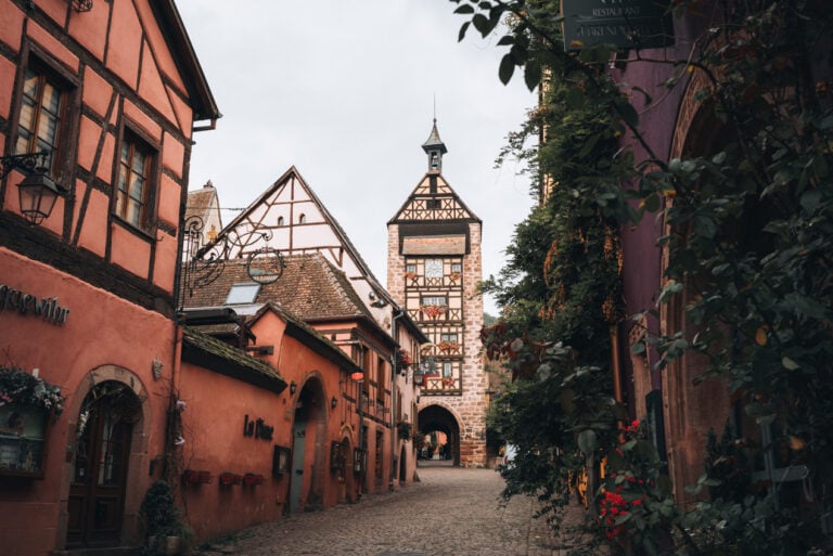Quiet early morning on Rue du Général de Gaulle in Riquewihr with empty cobblestone streets, colorful half timbered houses, and flower filled windows.