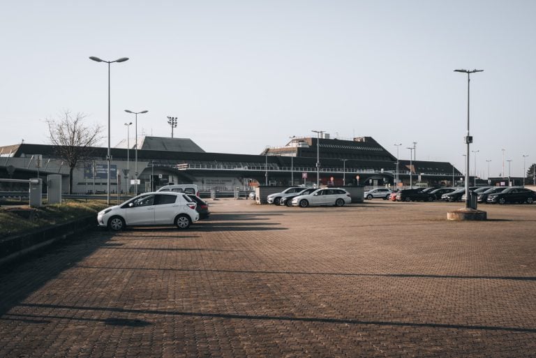 This is the parking lot and main entrance to the Strasbourg Airport. There is the main building and cars are parked in the lot.