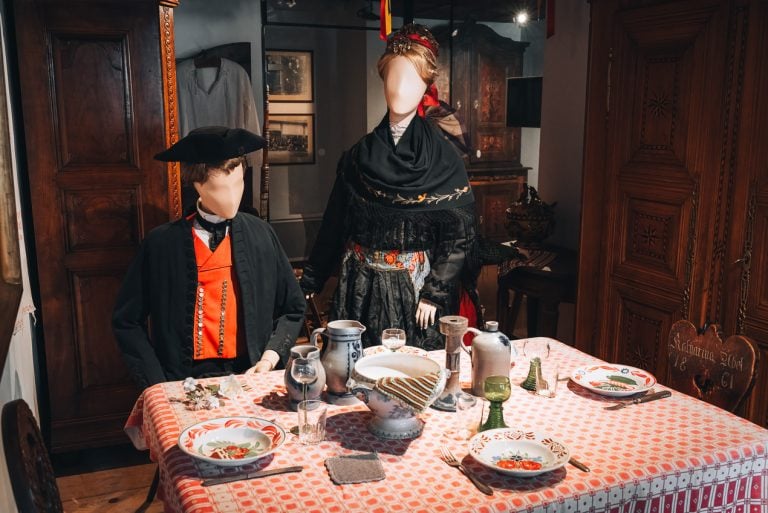 This is an exhibit a the Alsatian museum. It shows two figures dressed in traditional clothing eating at a table from the 18th century.