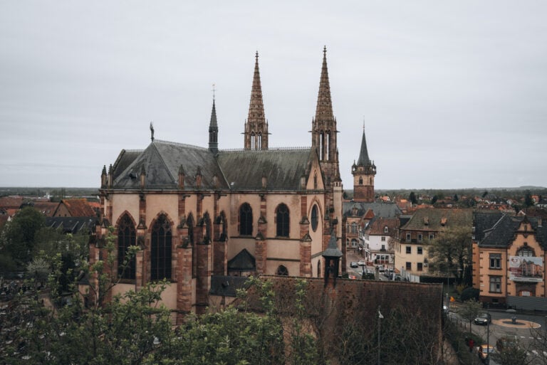 Exterior view of Saints Peter and Paul Church in Obernai with tall stone architecture and a prominent spire rising above the town. The historic church sits within the medieval streets of Obernai.