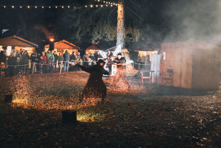 Two people dressed in black robes are holding flaming ropes and dancing around in the dark at the Christmas market in Wissembourg.