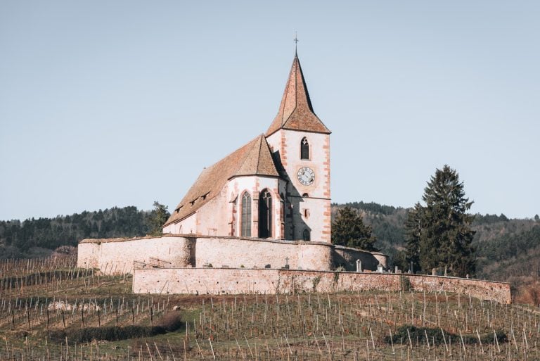 This is the Fortified Church in Hunawihr. It's half way between Ribeauvillé and Riquewihr. It has a clock tower and is surrounded by vineyards.