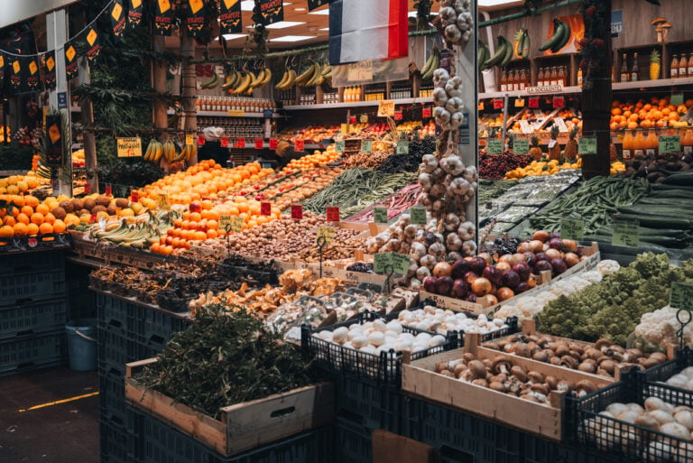 Colorful display of fresh fruits and vegetables inside Les Halles de Lyon Paul Bocuse market with neatly arranged stalls and abundant seasonal produce. The indoor food hall is a major culinary stop when in Lyon.