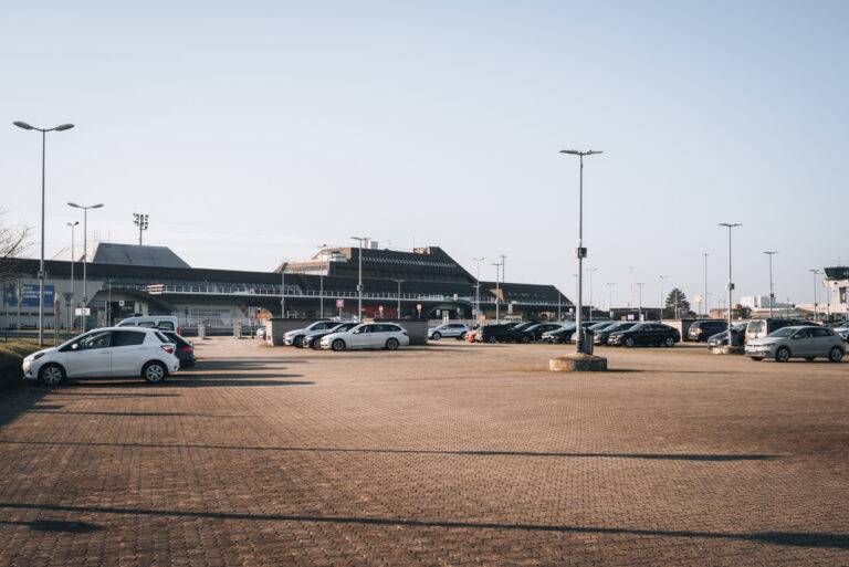 This is the front of the Strasbourg Airport. Cars are parked and people are entering the airport.
