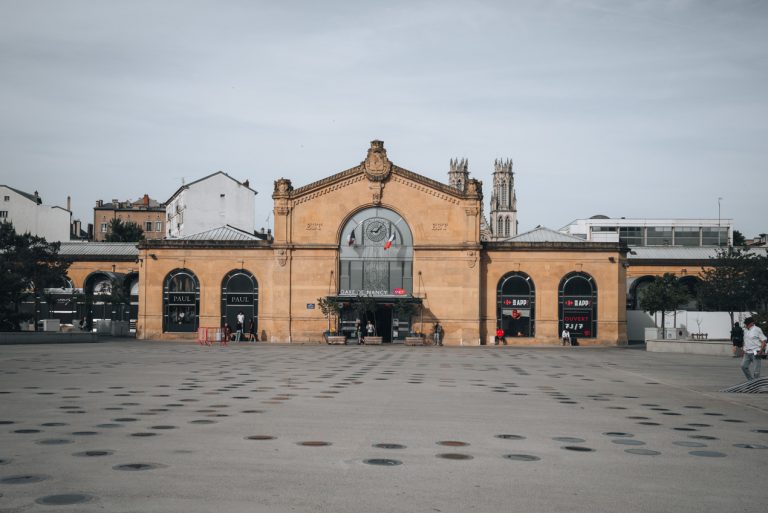 This is the front of Nancy's train station Gare de Nancy. There is one entrance and people are walking around.
