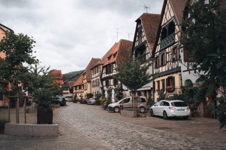 Grand Rue in Bergheim lined with pastel half timbered houses, flower boxes, and cobblestone streets under a bright sky.