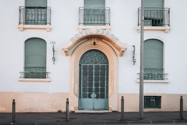 This is the exterior of Hôtel Peron. There are five windows and one door. The name of the hotel is written above the door.