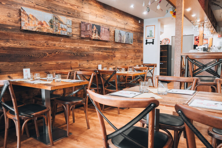 Inside La Soi restaurant in Colmar. There are wooden tables and chairs, and painting on the wall. The tables are set with traditional Alsatian table clothes.