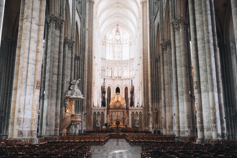 A row lined with wooden chairs on either side leads to the golden altar in the Amiens Cathedral. This is one of the many churches to see in France.