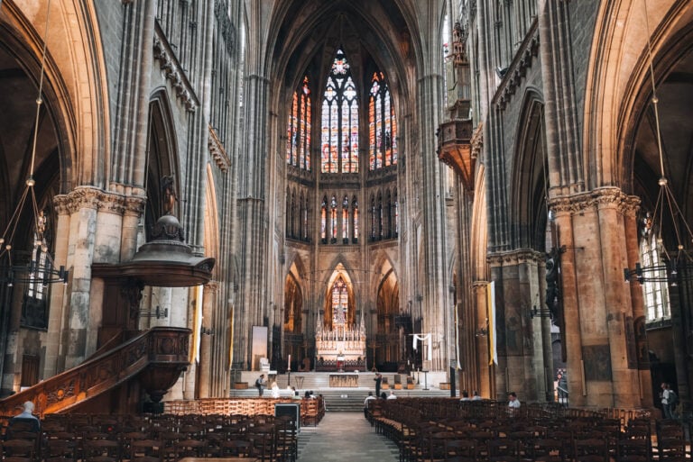 A row surrounded by wooden chairs lead to the altar, surrounded by stained-glass windows, inside the Metz Cathedral.