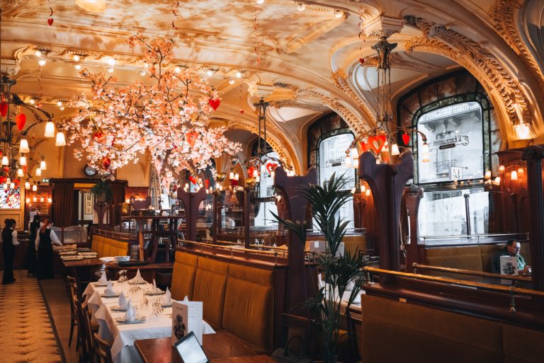 This is the inside of the Brasserie Excelsior in Nancy. You can see the table with separators that are decorated with wood carvings. The ceiling also has very detailed carvings.