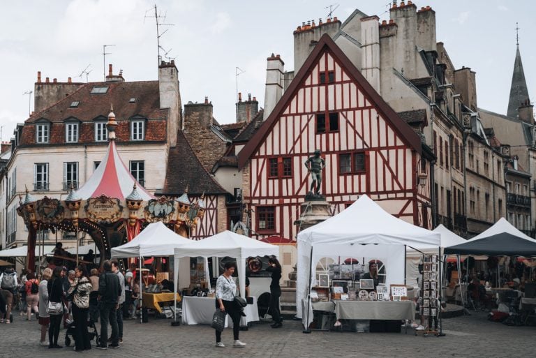 This Place François Rude. There is a red half-timbered house, a merry-go-round, and a small market with people shopping. It's one of the reasons why Dijon is worth visiting.