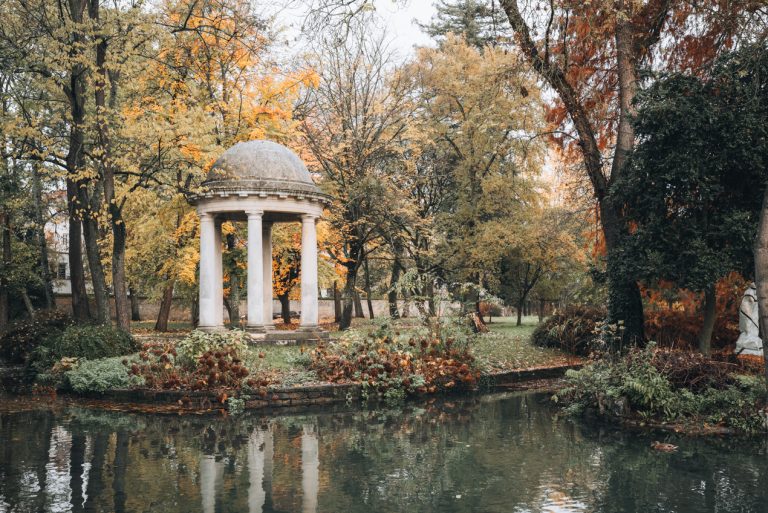 This is the Jardin Botanique de l'Arquebuse in Dijon. There is a small reservoir and surrounding it are gardens and tall trees. In the center there is a small gazebo. 