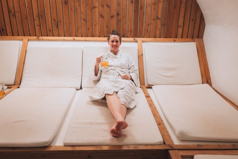 This is a Jen Ciesielski in the relaxation room at Taaka Beer Spa. She is in a white robe and sitting on a lounge chair holding a pint of beer.