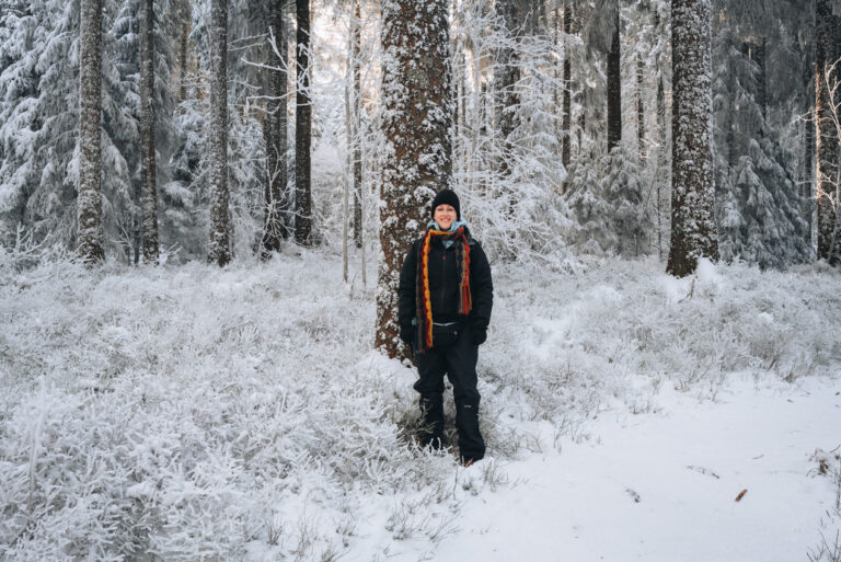 Jen Ciesielsi standing on a hiking and snowshoe trail at Champ du Feu in winter. There are is on the ground and she is dressed warmly. 