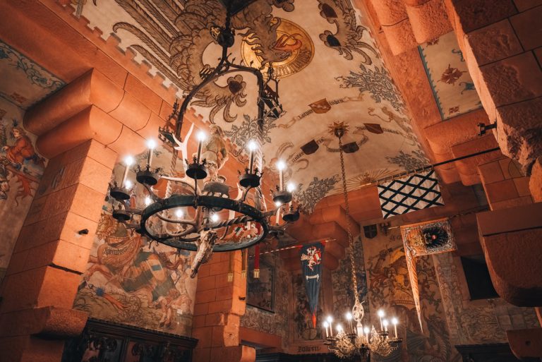 This is the Kaiser Room at the Haut Koenigsbourg Castle. This is the ceiling and there are two lamps and paintings. Then on the walls there are tapestries. 