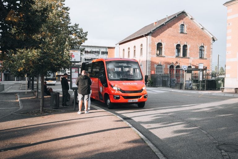 This is the Kutzig bus in front of the train station in Colmar. It's parked and people are in line boarding the bus.