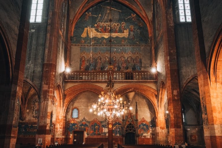This is the La Navicella mural at the Église Protestante Saint Pierre le Jeune in Strasbourg. It's a large religious painting of Jesus Christ on the back of the church and there is a lamp in front of it.