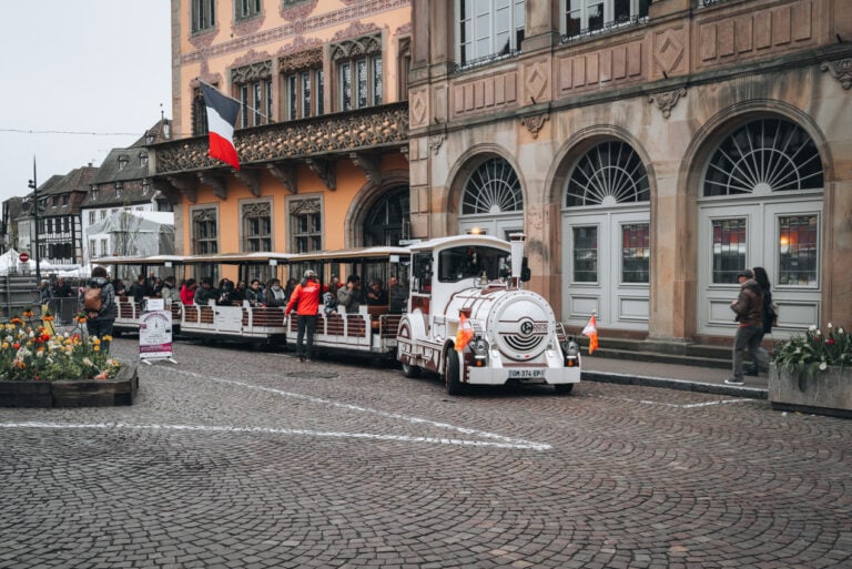 The Obernai Little Tourist Train parked in front of the town hall with passengers seated inside as the conductor prepares for departure. The small sightseeing train offers a relaxed way to see the main landmarks around town.