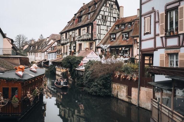 This is Little Venice in Colmar at Christmas. There is the canal with a gondola in the middle and on either side there are half-timbered houses decorated with ornaments.