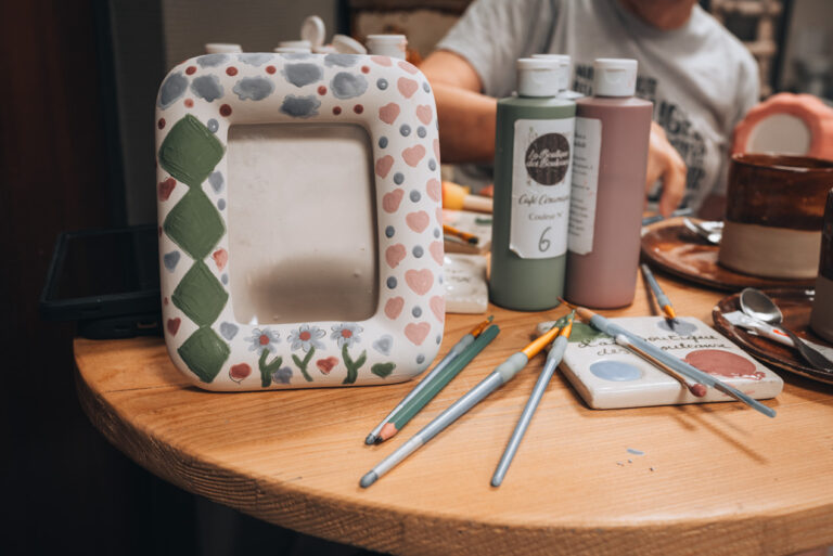 A painted picture frame surrounded by paint brushes and paint. This is Jen's picture frame that she made at La Boutique des Bouleaux in Strasbourg.