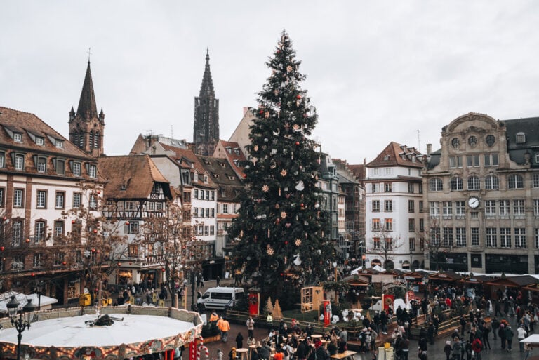 Panorama of Place Kléber from the Aubette 1928 during Strasbourg's Christmas market. In the center there is the Christmas tree surrounded by wooden chalets selling food and people wandering around.