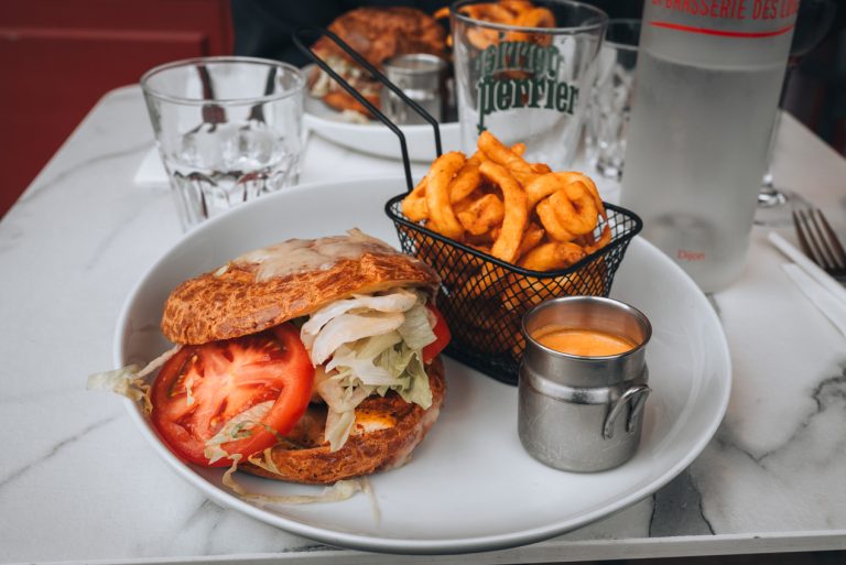 This is my giant gougère sandwich from La Brasserie des Loges in Dijon. It's a traditional cheese puff filled with chicken, tomatoes, and lettuce. There is a side of fries and mustard.