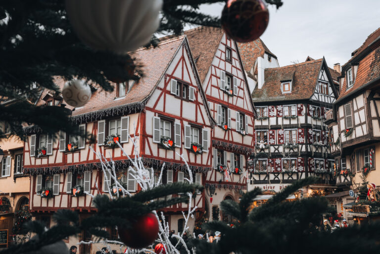 Red half-timbered houses at the intersection of Grand Rue and Rue des Marchands at Christmas time in Colmar. Each is covered in Christmas decoration and lights.