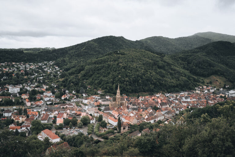 Panorama of Thann from the Croix du Rangen with the rooftop visible in the foreground and the tree covered Vosges in the distance.